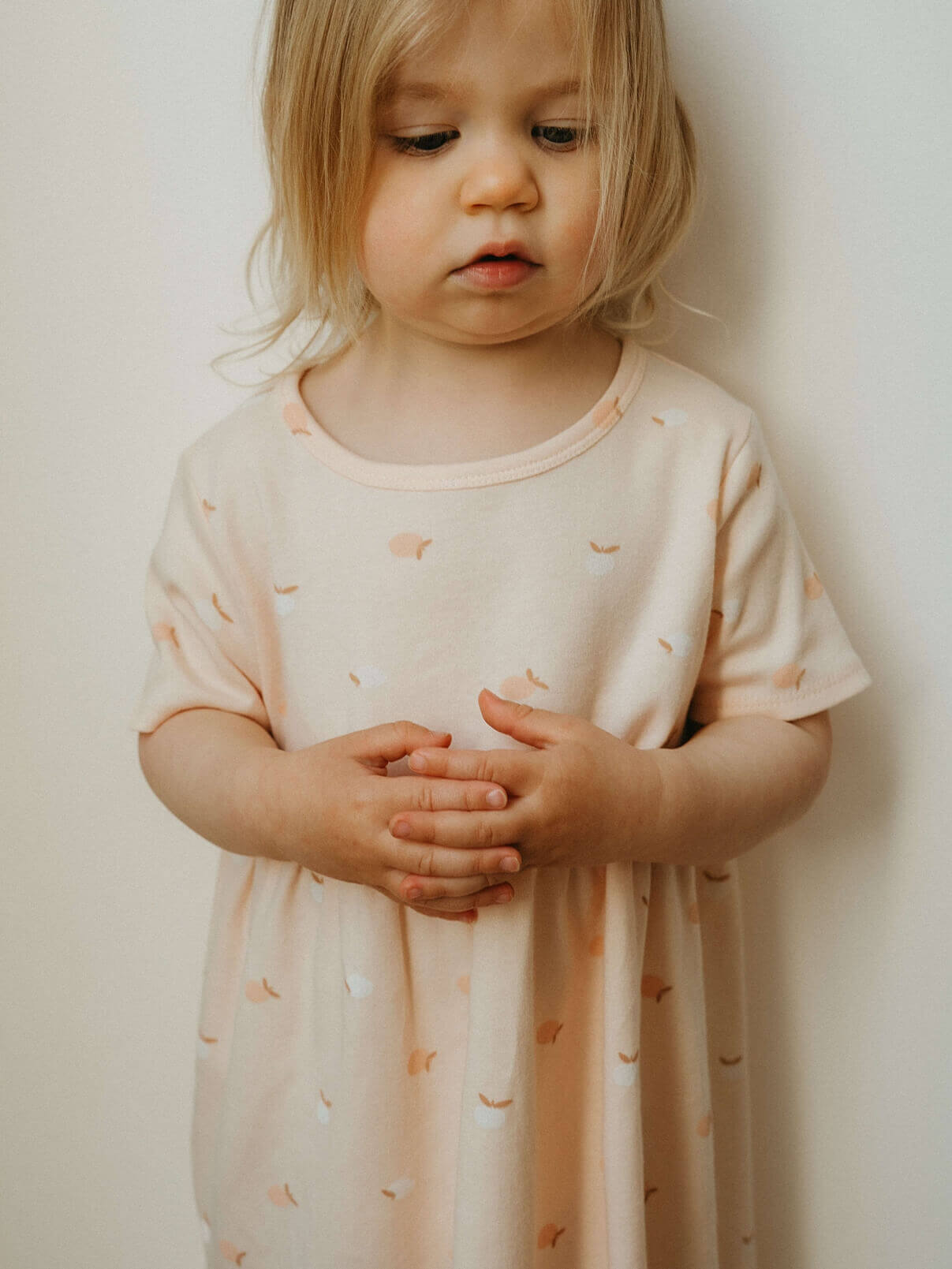 Young child wearing a light pink dress with small patterns against a plain background
