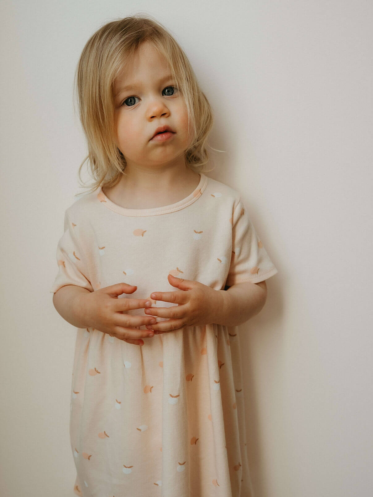 Young child wearing a light-colored dress with small patterns against a plain background