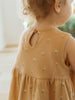 Child wearing a mustard yellow dress with floral patterns, standing indoors.