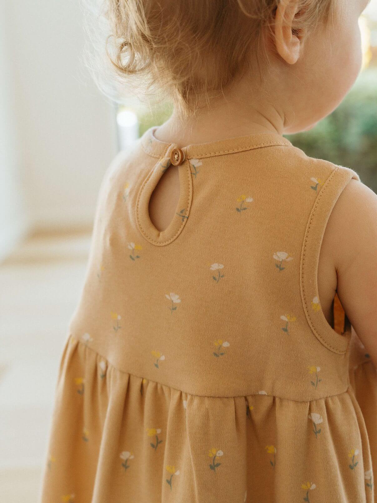 Child wearing a mustard yellow dress with floral patterns, standing indoors.