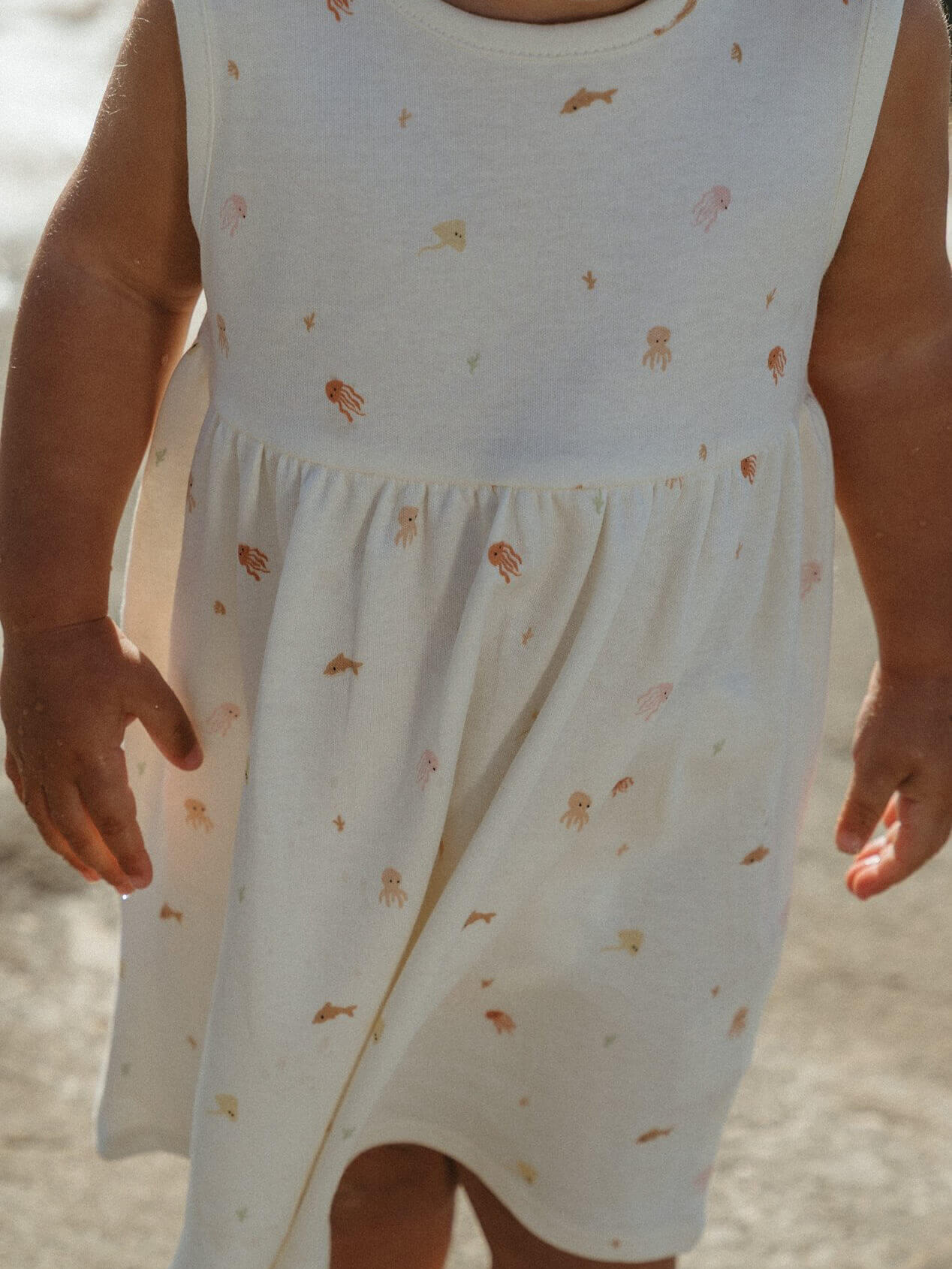 White sleeveless dress with small patterns worn by a child, against a neutral background