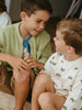 Two young boys sitting on the floor, smiling and looking at each other.
