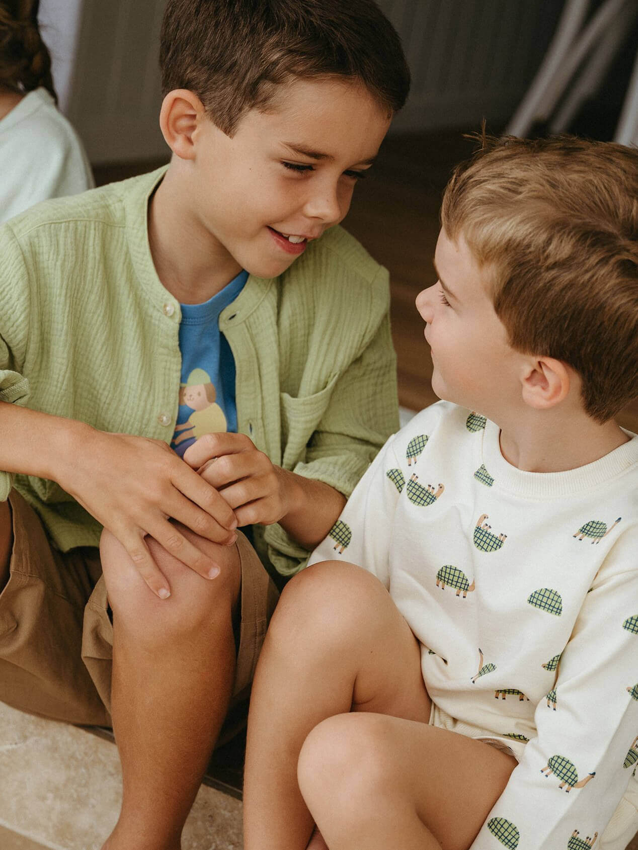 Two young boys sitting on the floor, smiling and looking at each other.