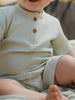 Child wearing a light-colored ribbed shirt and shorts sitting outdoors.