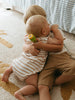 Two children hugging on a carpeted floor with a striped rug in the background.