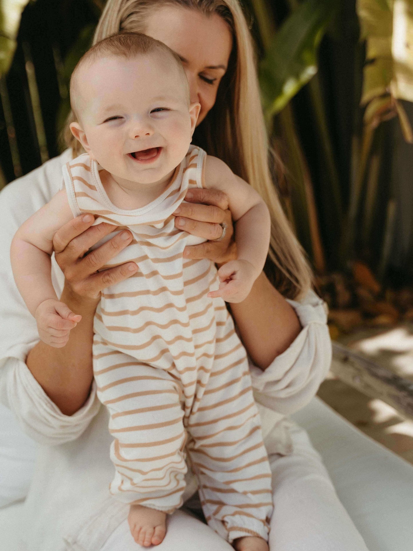 Woman holding a baby wearing a striped onesie with a blurred natural background