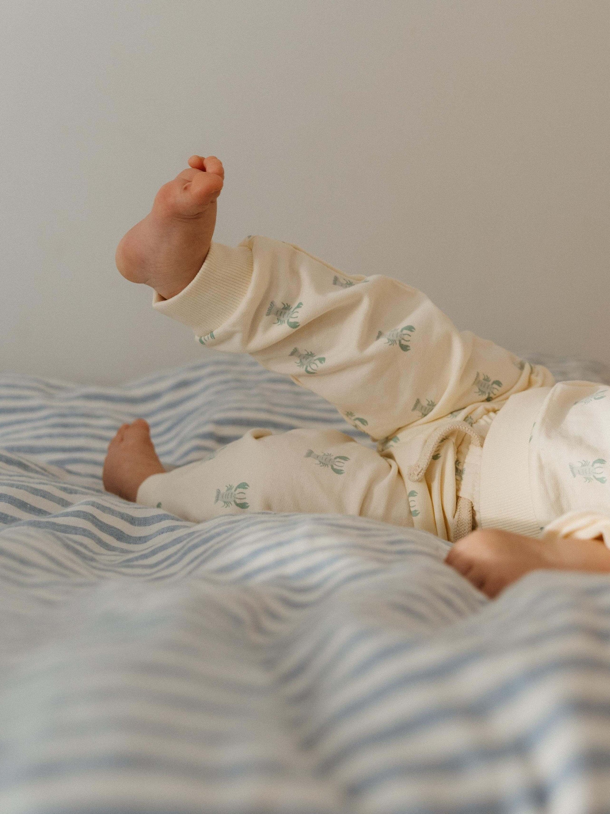 Baby playing with his feet on the bed.