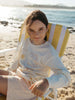 Girl sitting on a yellow striped beach chair wearing a floral summer shorts and a white long sleeve tee