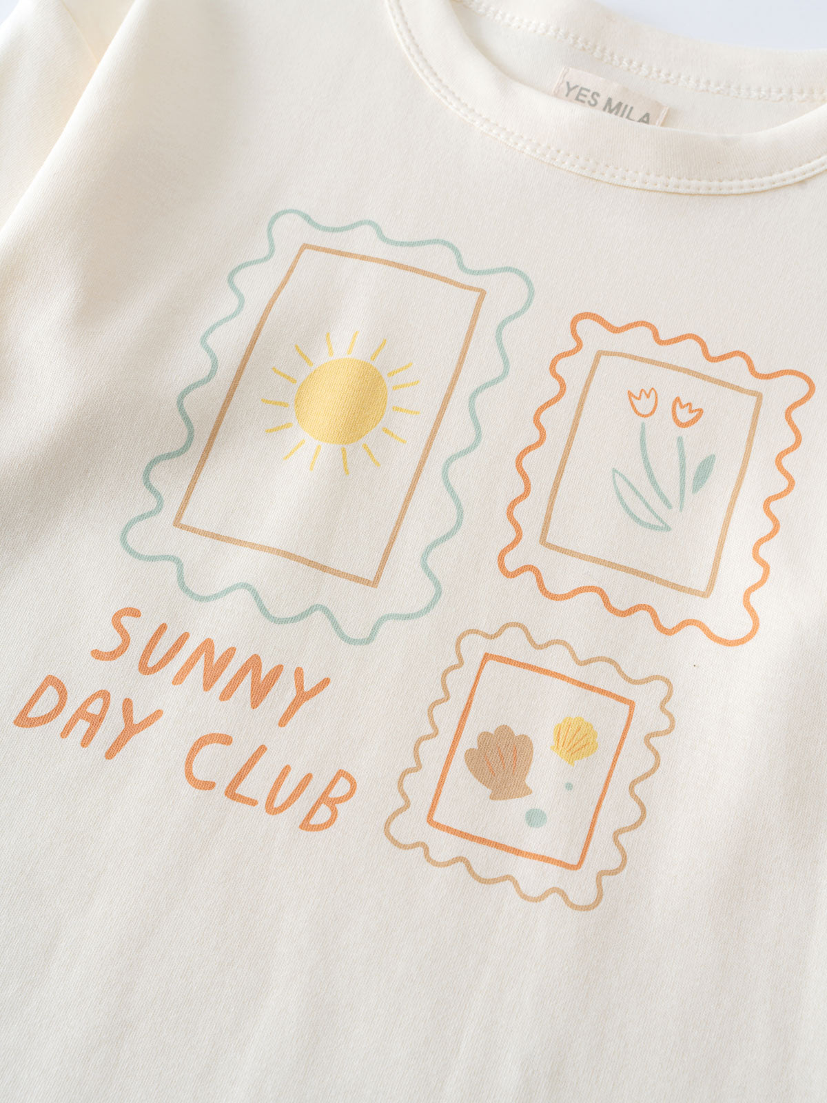 Close-up of a cream-colored shirt with three postage stamp graphics and text Long Sleeve Tee - Sunny Club Day Girls