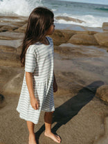 Young girl in a striped dress standing on a rocky beach with ocean waves in the background