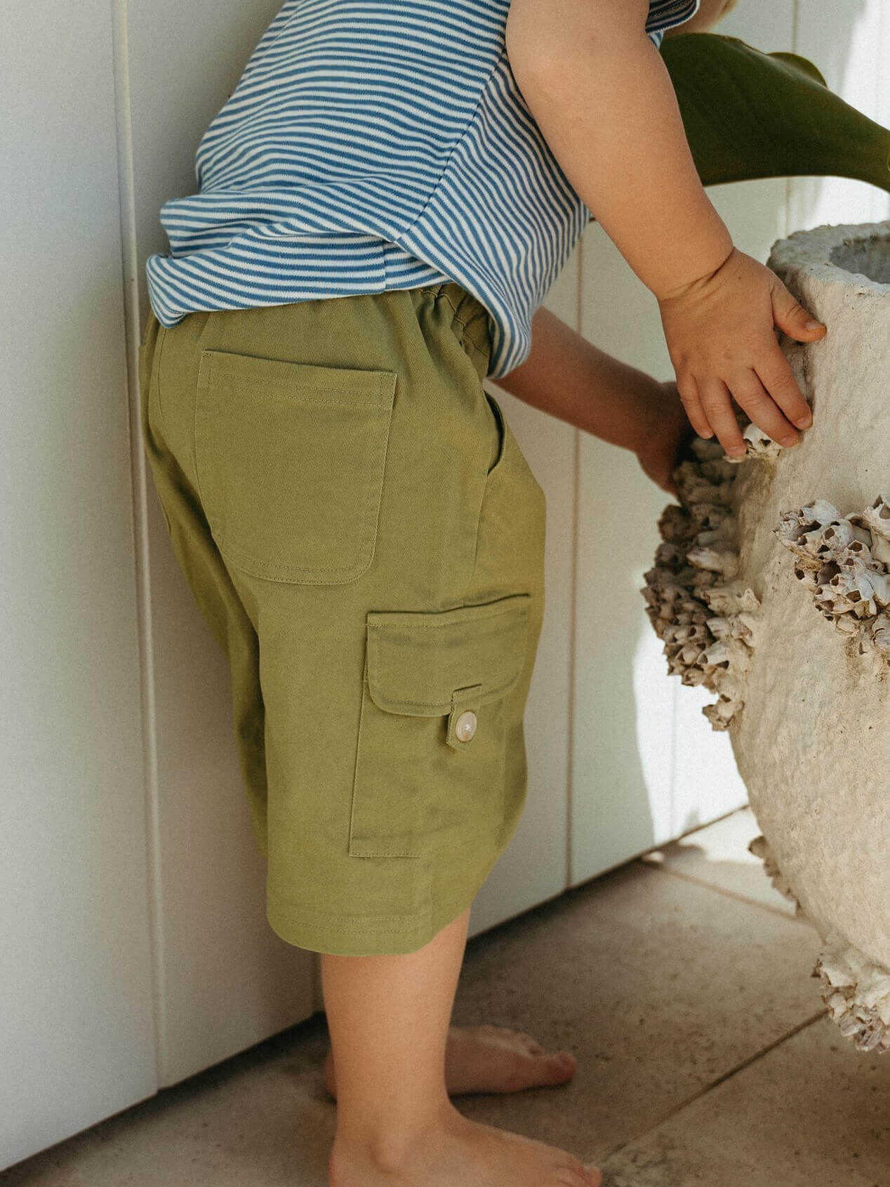 Child wearing green shorts and a striped shirt interacting with a stone object.