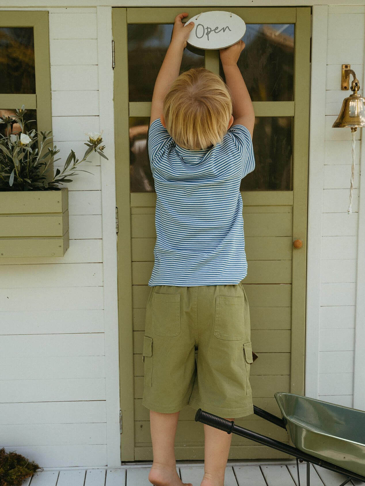 Child holding a 'Open' sign on a door with a white house exterior.