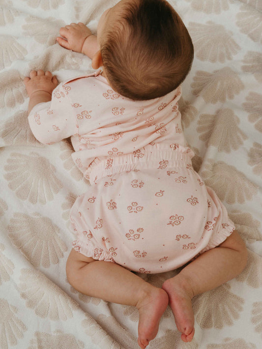 Baby in a pink floral outfit lying on a patterned blanket