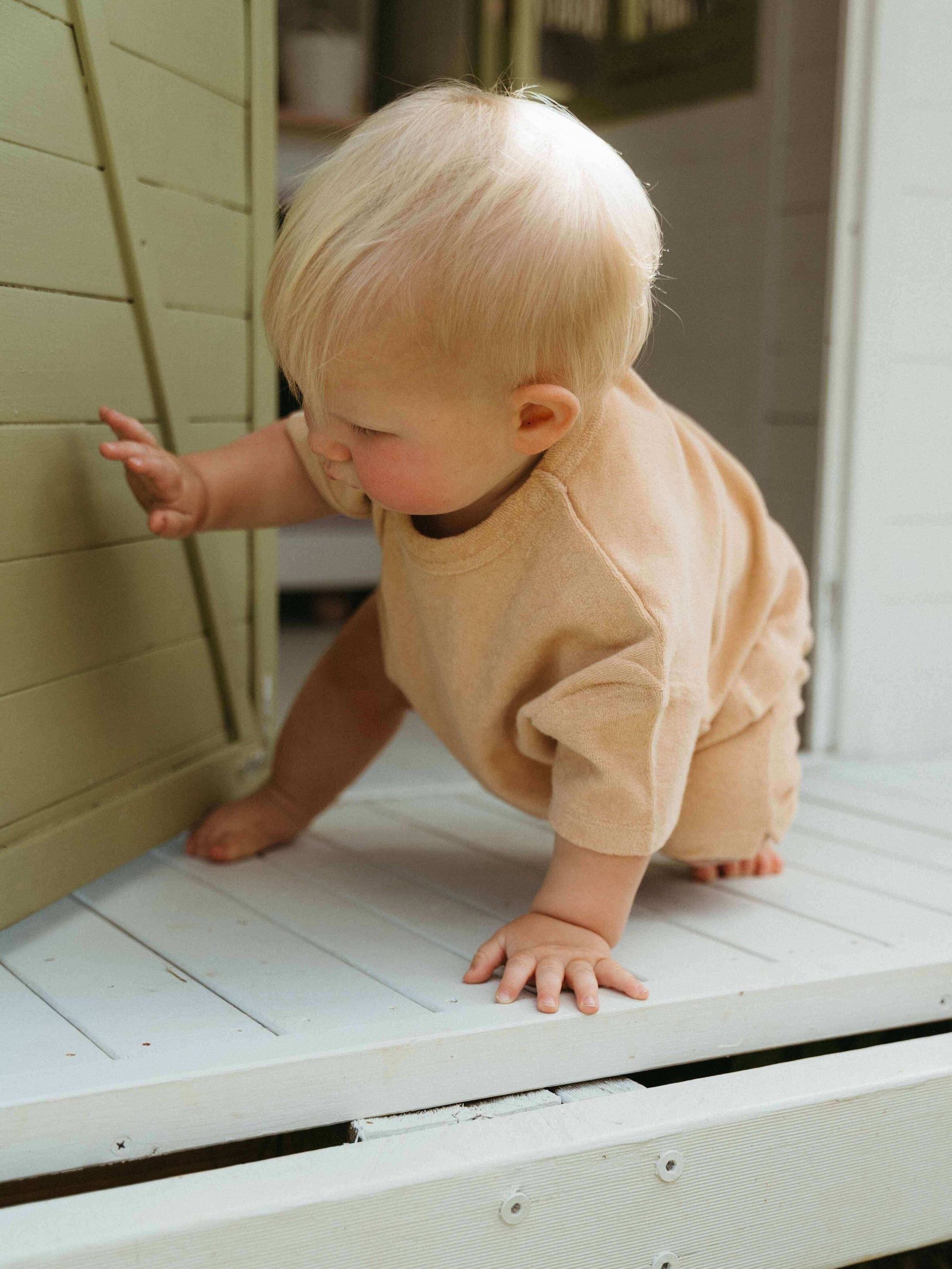 Baby in a beige outfit crawling on a wooden surface.