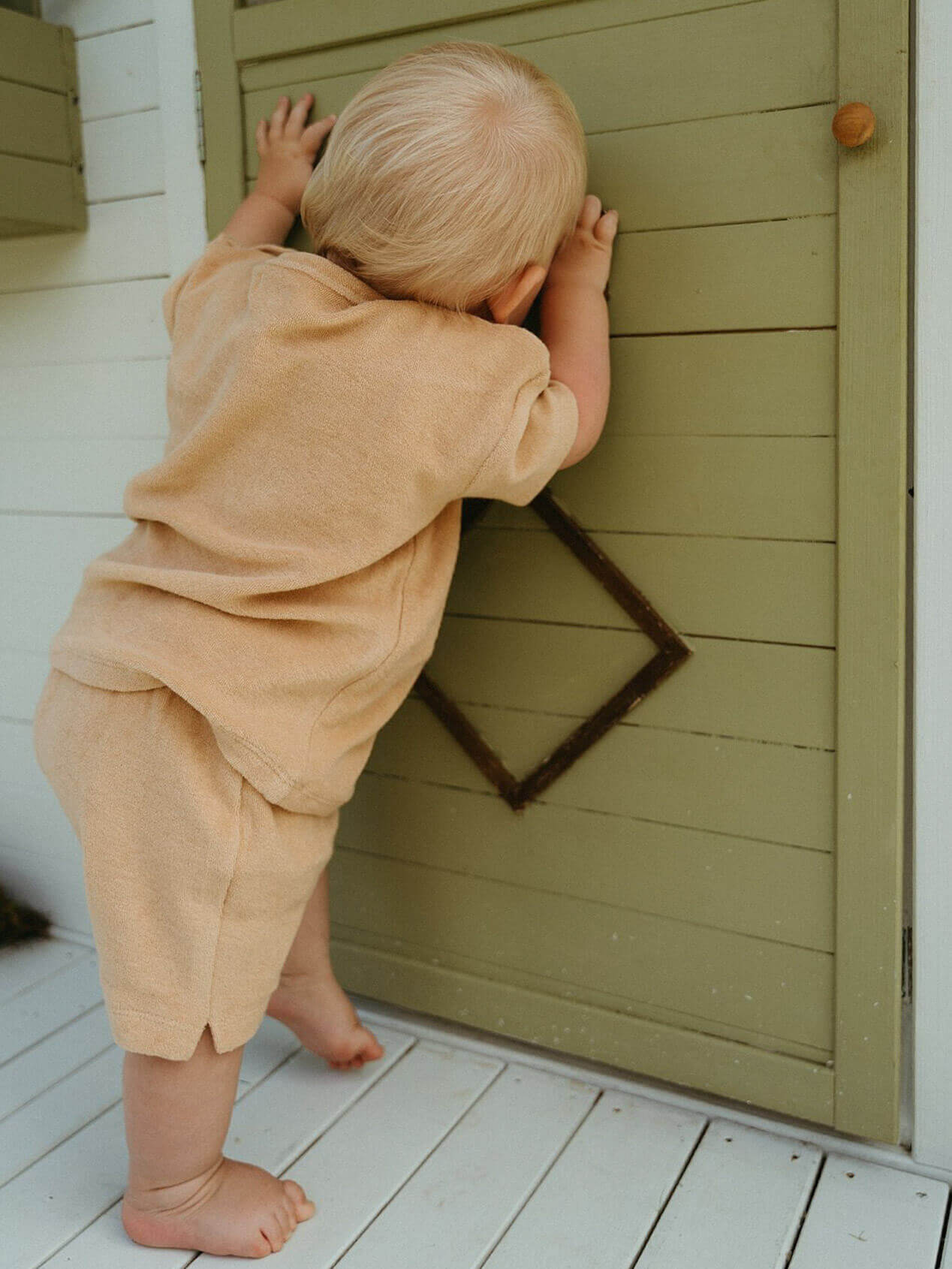 Child in beige outfit climbing a wooden door