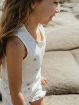 Young girl in a white sleeveless dress with floral patterns sitting on a stone surface.