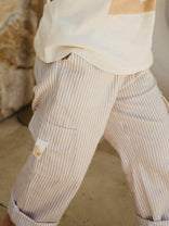 Close-up of a child wearing beige and white striped pants with a blurred background.