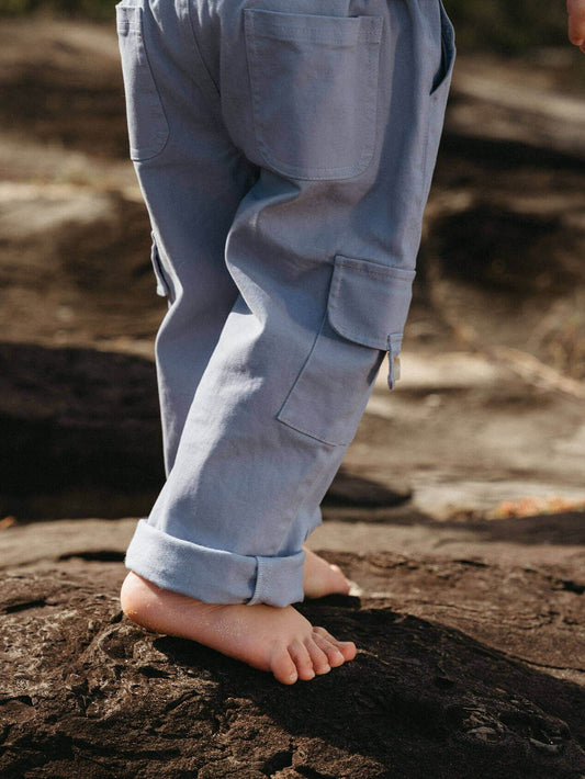 Boy wearing light blue cargo pants standing on a rocky surface.