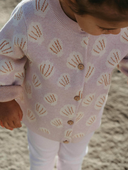 Child wearing a light purple cardigan with shell pattern on a sandy background