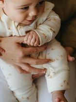 Baby in a white outfit with small patterns held by an adult's hands.