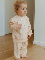 Child wearing a light pink outfit with small patterns indoors on a wooden floor.