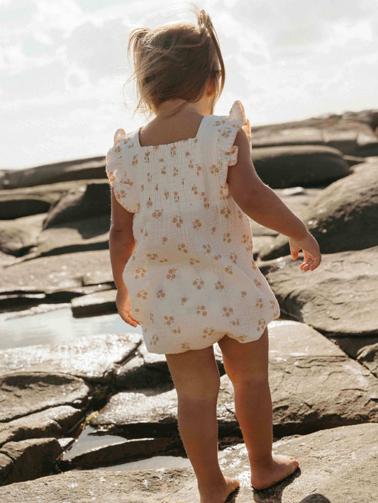 Child in a floral romper standing on rocky terrain near water