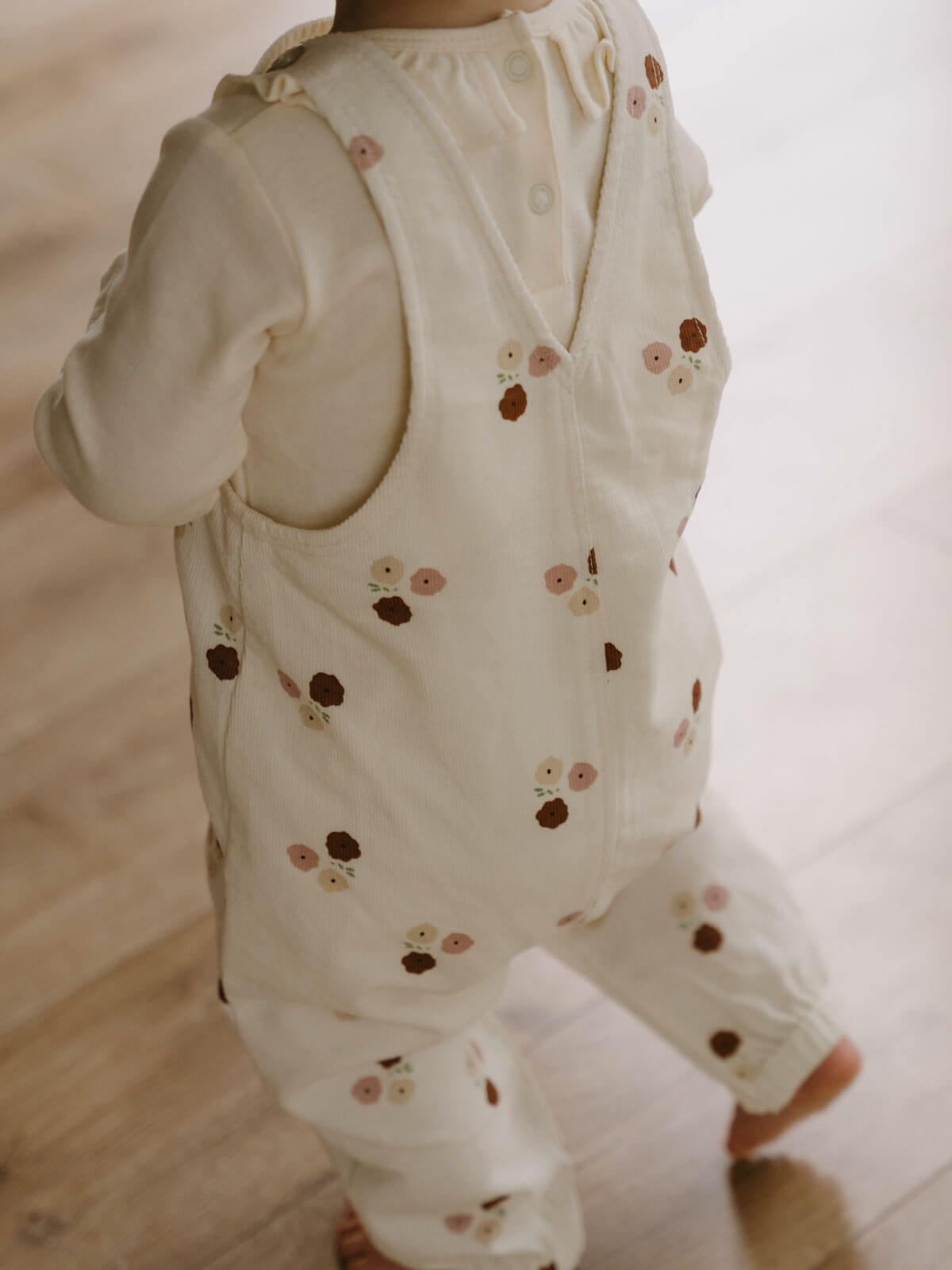 Baby wearing cream overalls with floral embroidery, sitting on beige surface Printed Overalls - Autumn Bouquet Ecru Baby girl
