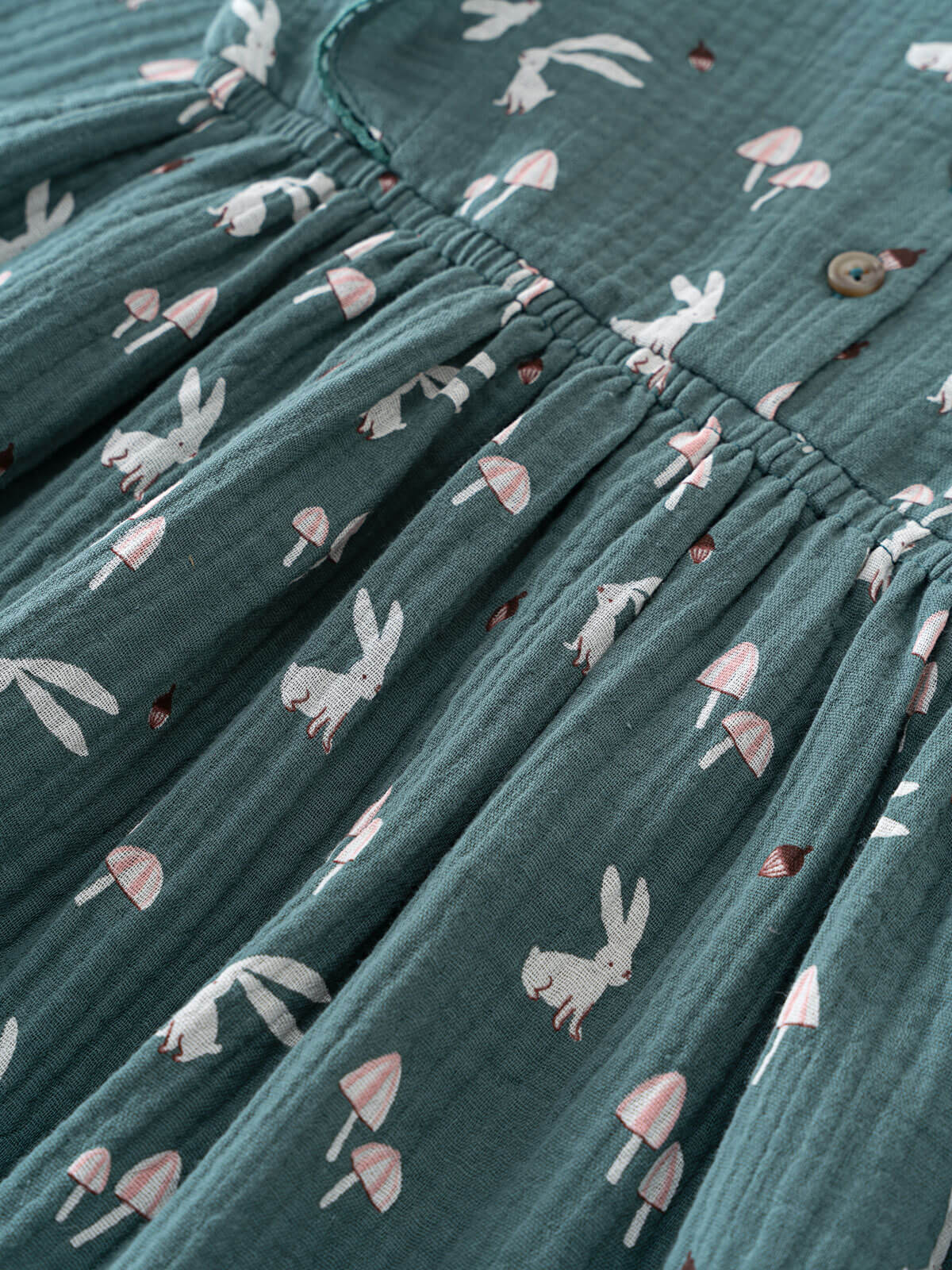 Textured dress fabric with a pattern of rabbits and mushrooms on a teal background