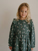 Young girl wearing a green dress with a pattern of small figures against a plain background