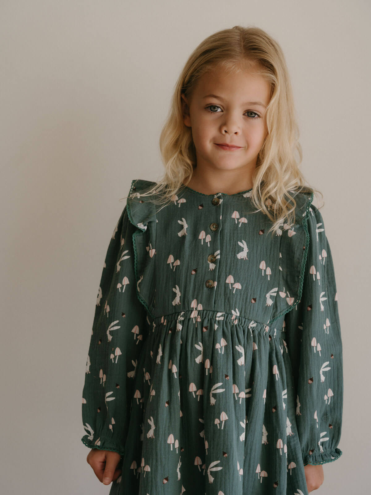 Young girl wearing a green dress with a pattern of small figures against a plain background