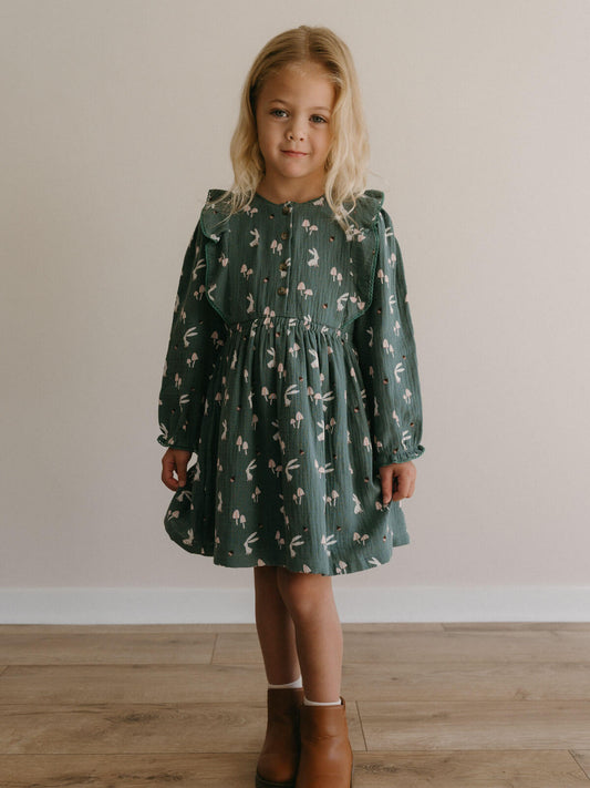 Young girl wearing a green dress with a floral pattern against a plain background