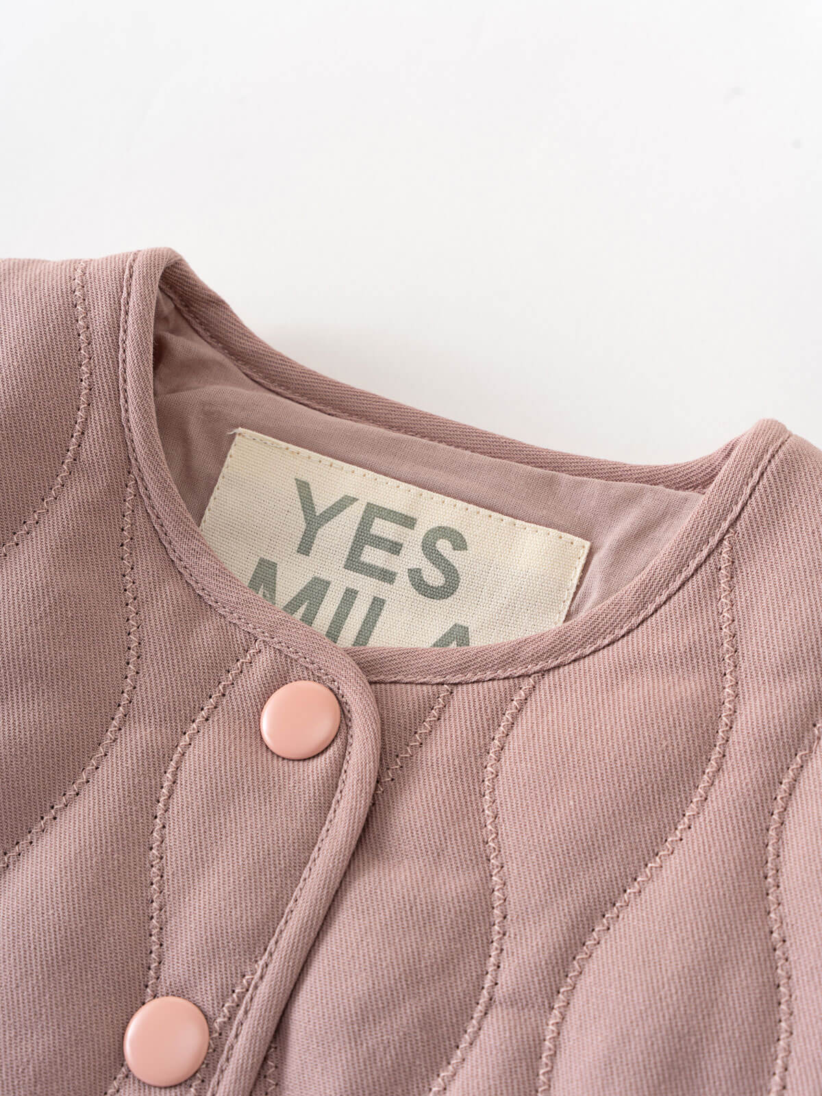 Close-up of a baby outfit with pink buttons and a visible label on a white background Quilted Jacket - Blush Baby girl