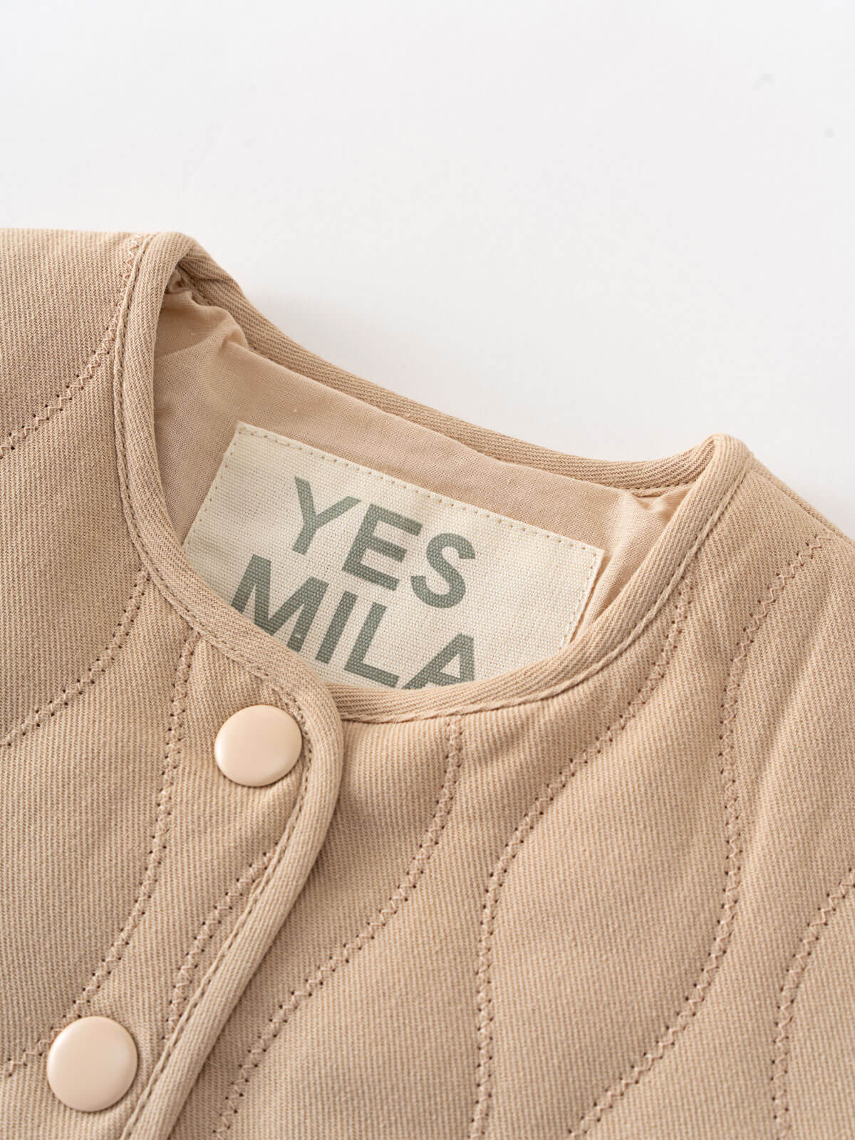 Close-up of a beige garment with a 'YES MILA' label on a white background Quilted Jacket - Clay Baby girl