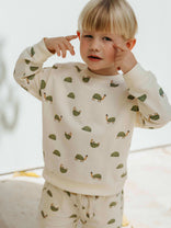 Child wearing a cream-colored sweatshirt with green animal prints on a white background
