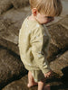 Child wearing a light green outfit with cloud patterns on a stone surface