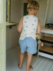 Child wearing a sleeveless shirt with blue patterns and light blue shorts in a room with wooden floors and white walls.