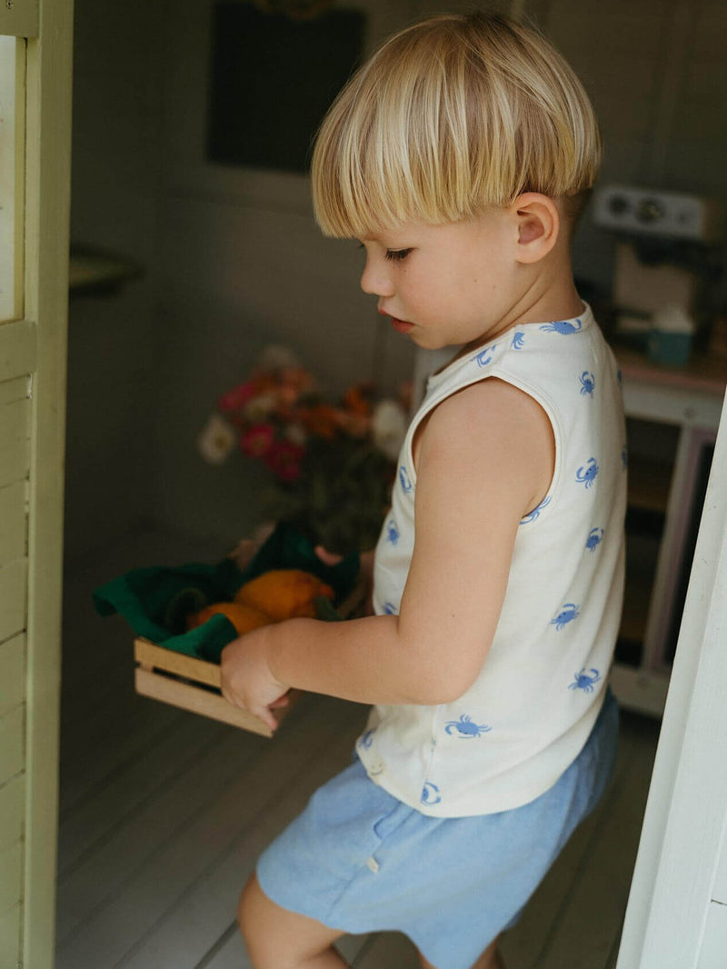 Child holding a wooden crate with vegetables in a kitchen setting