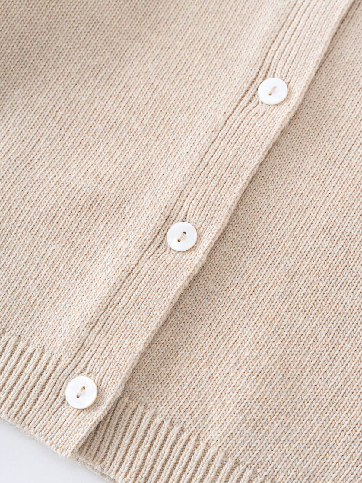 Close-up of a beige knitted cardigan with white buttons on a light gray background Ruffle Cardigan - Ecru Girls