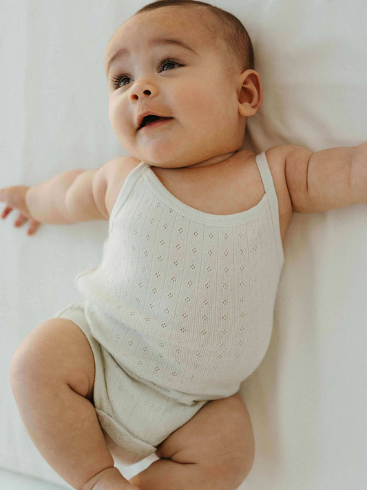 Baby wearing a light-colored sleeveless outfit on a white background