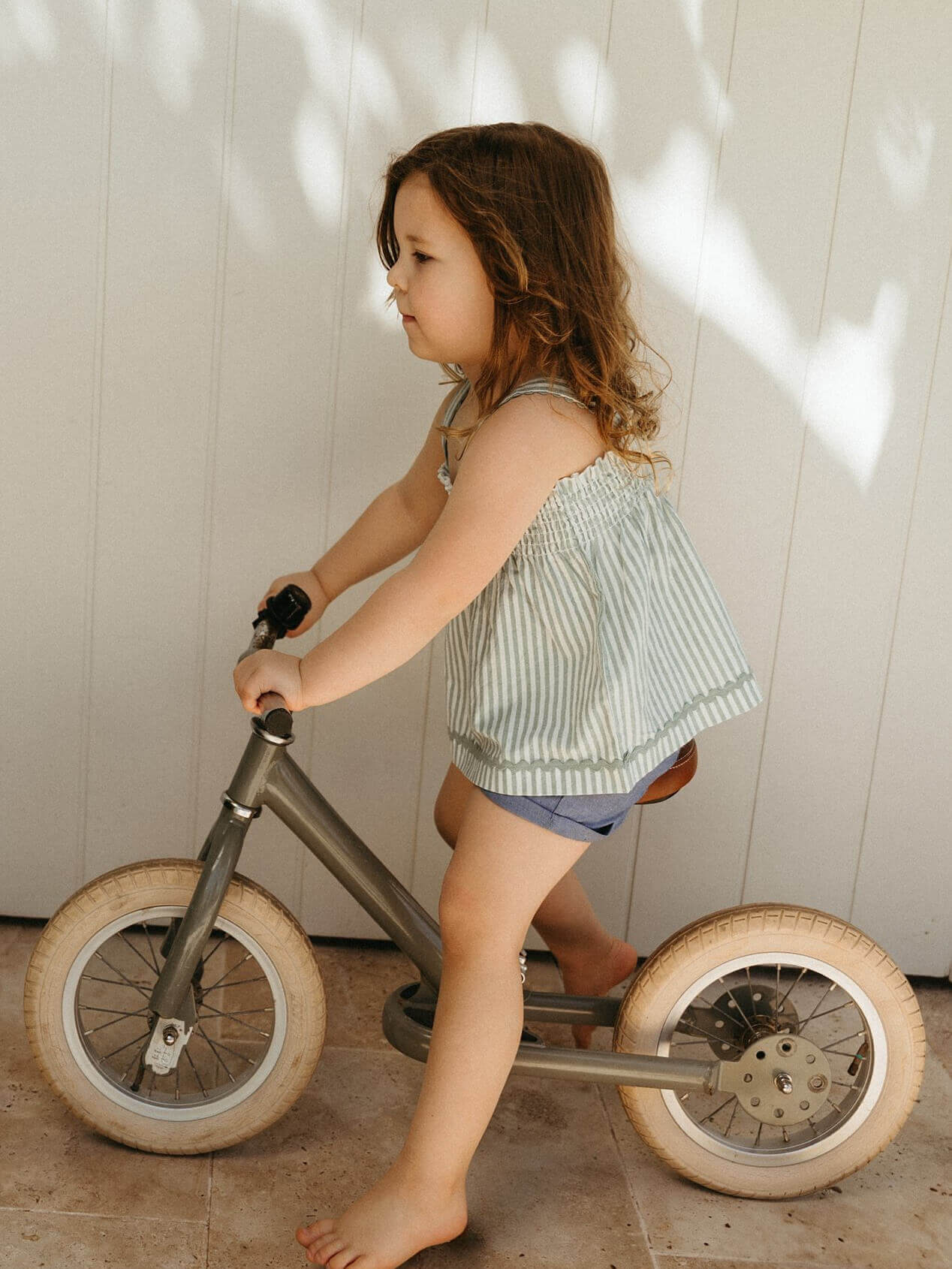 Child riding a balance bike indoors with a neutral background