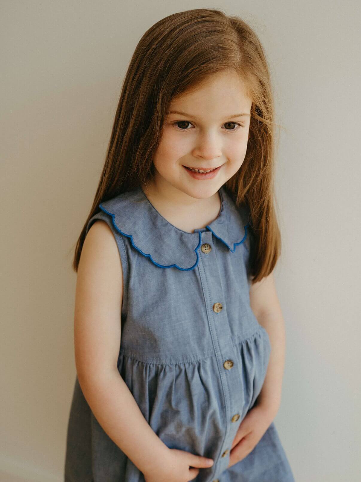 Young girl wearing a blue dress with a scalloped collar against a plain background