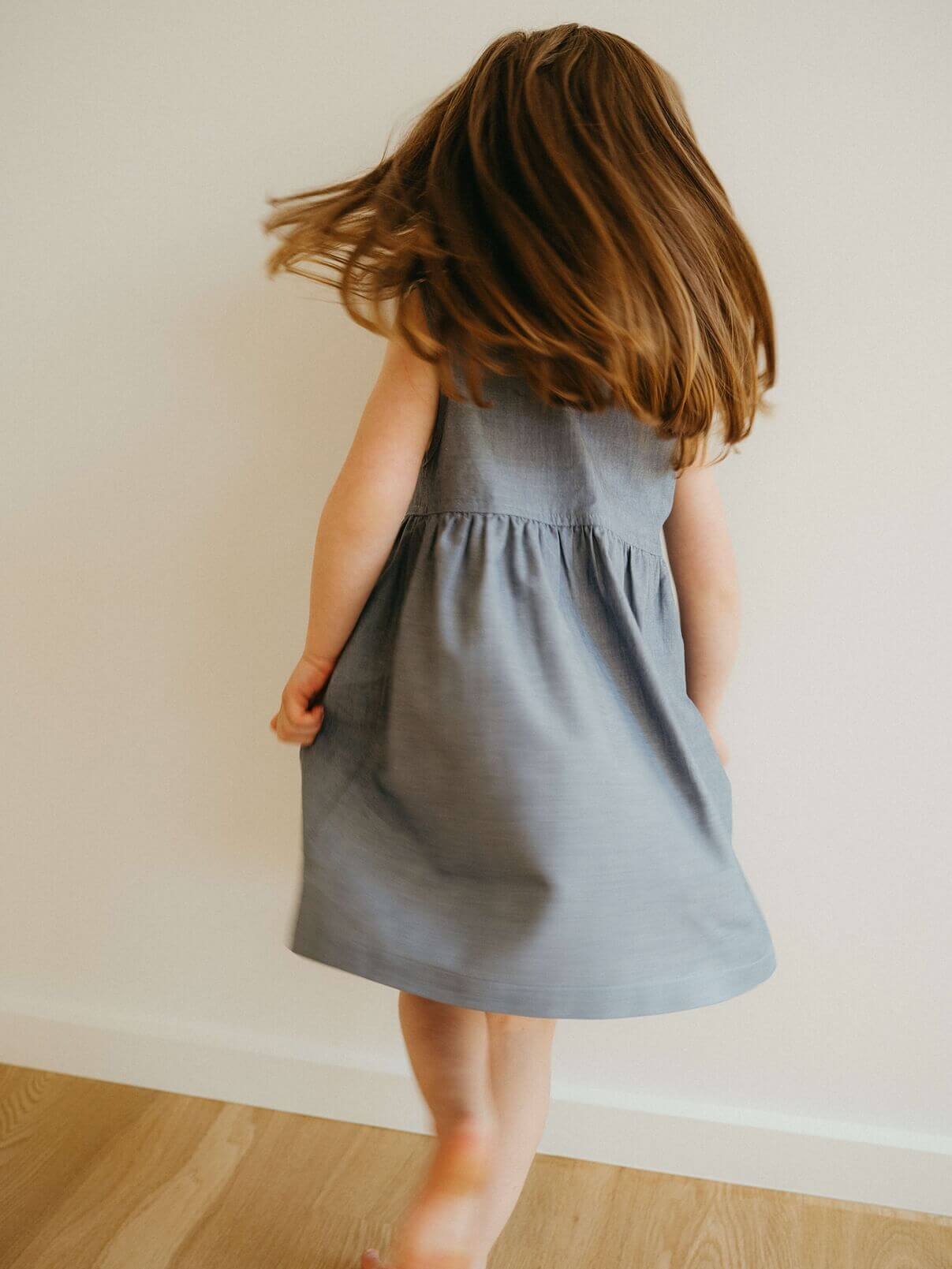 Child wearing a denim dress against a plain wall