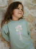 Child wearing a light blue sweatshirt with a floral design against a stone wall. Sophie Sweatshirt - Posy Mint Girls