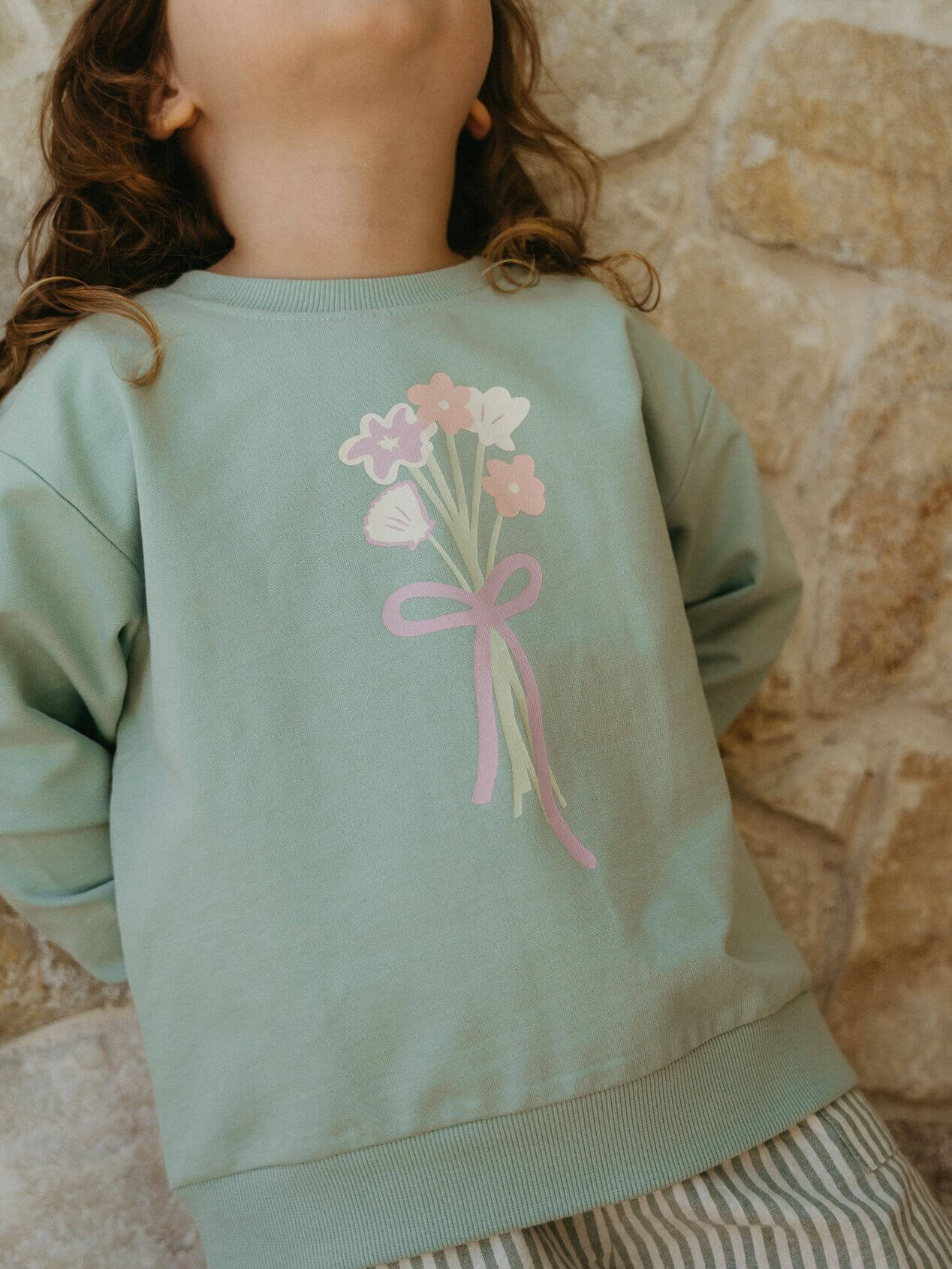 Light green sweatshirt with floral design worn by a child against a stone wall background Sophie Sweatshirt - Posy Mint Girls