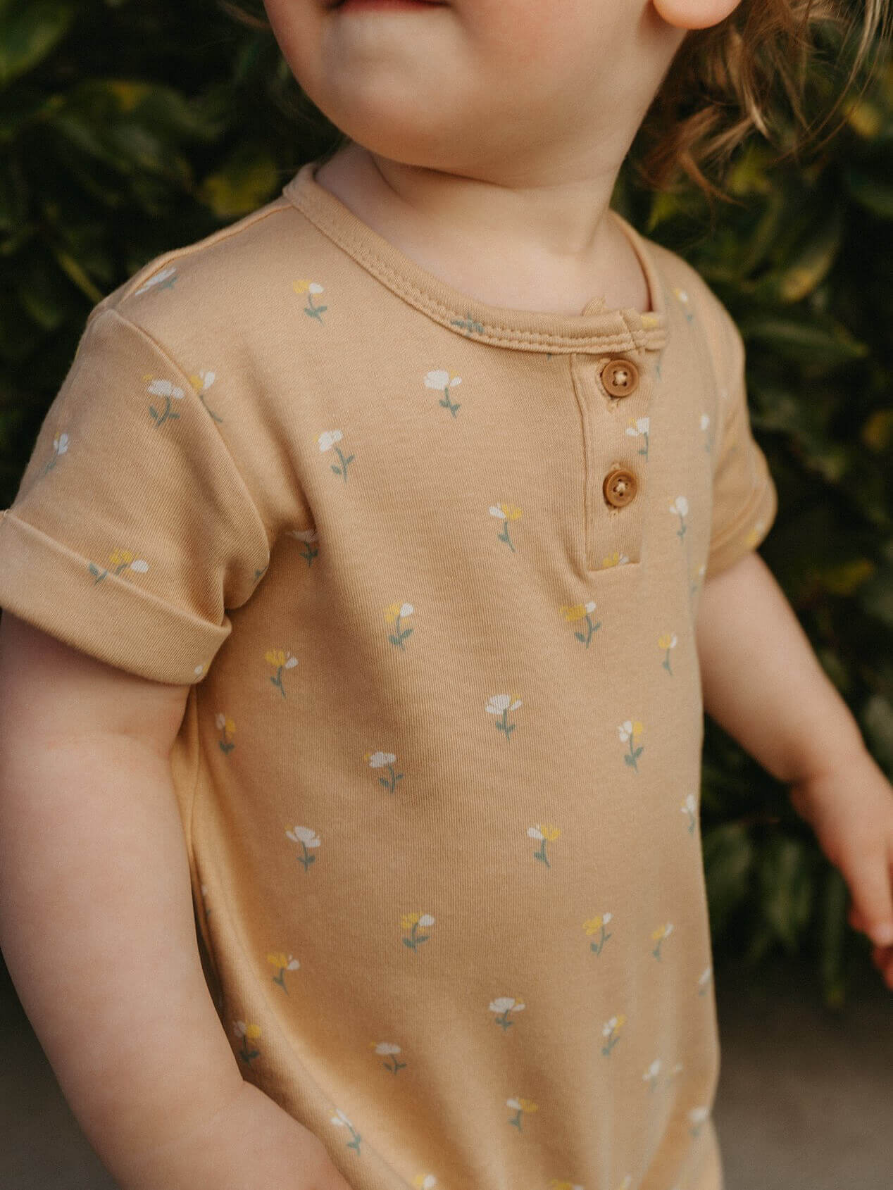 Child wearing a brown onesie with floral patterns against a blurred green background