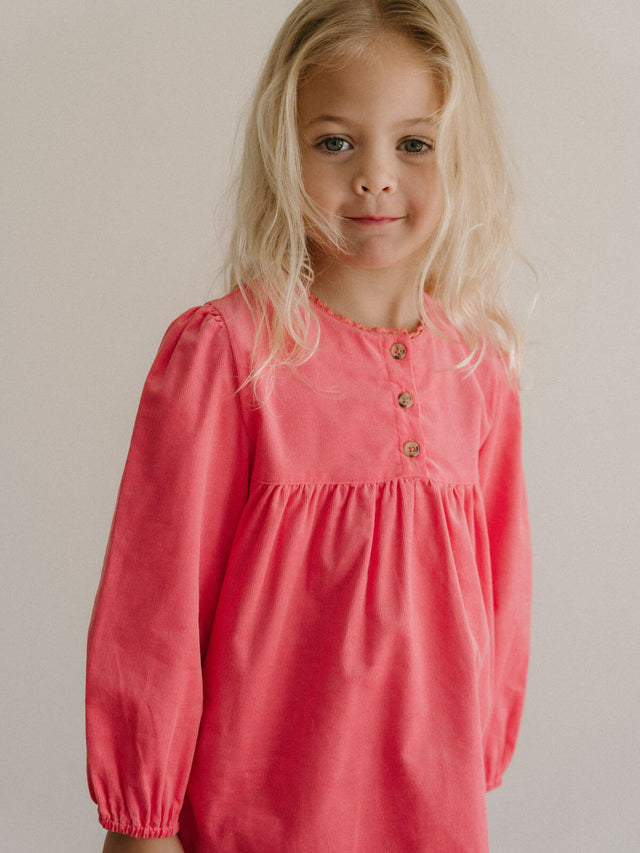 Young girl wearing a pink dress with long sleeves against a plain background