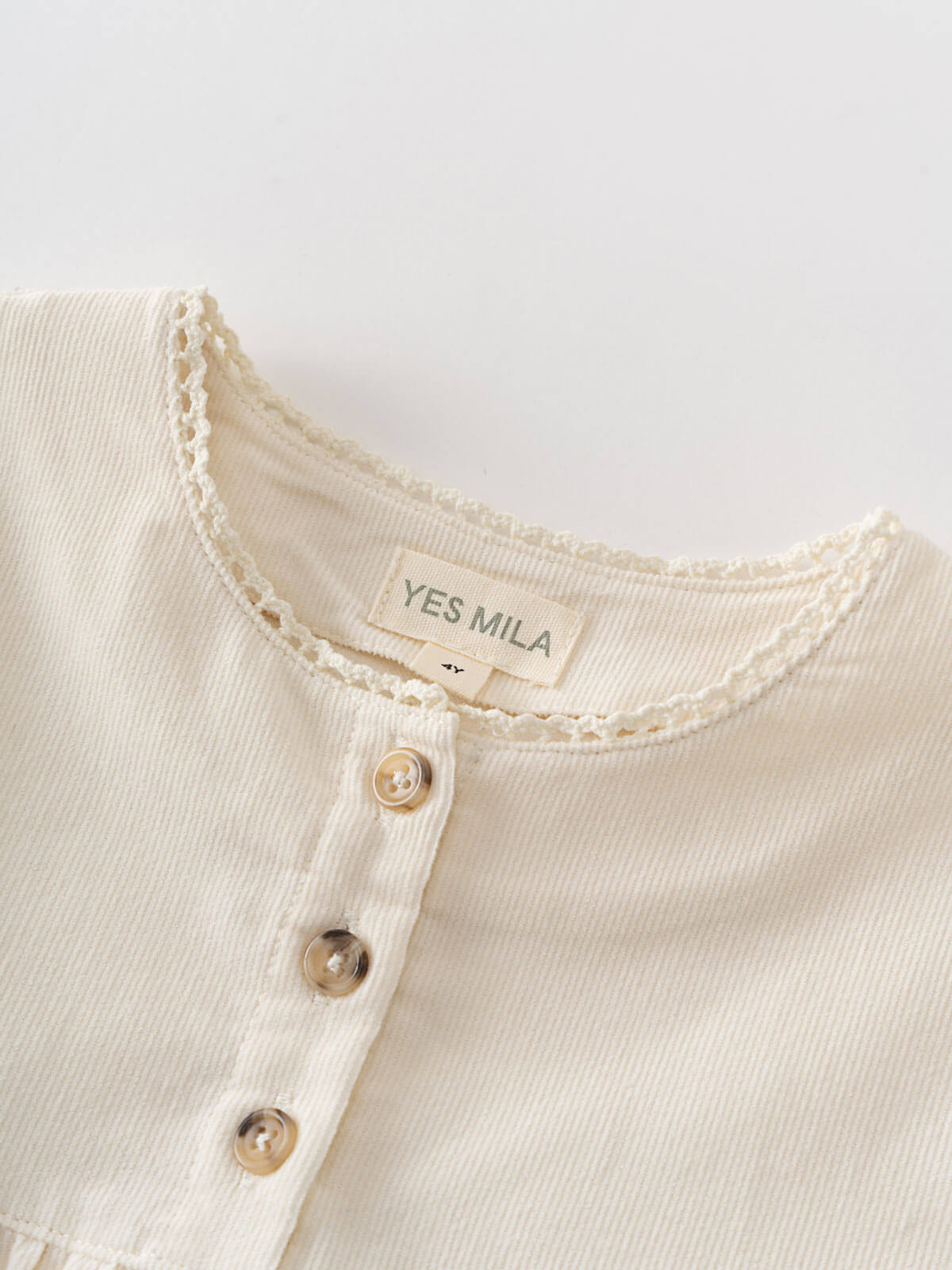 Close-up of a cream-colored garment with a 'YES MILA' label on a light gray background Three Button Blouse - Ecru Girls
