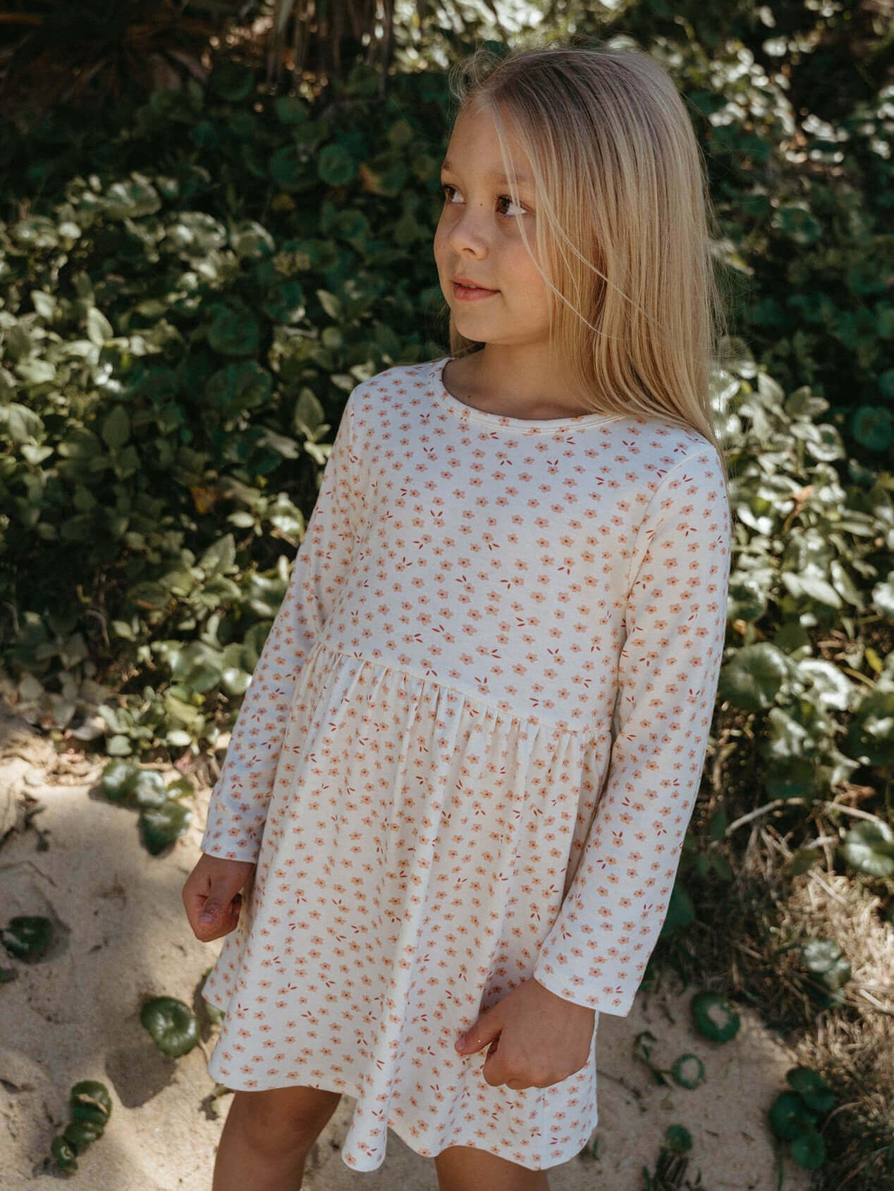 Young girl in a floral dress standing in a natural setting with greenery.