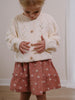 Young child wearing a cream cardigan and patterned pink skirt buttoning the sweater Woven Skirt - Bird And Blossom Rosehip Girls