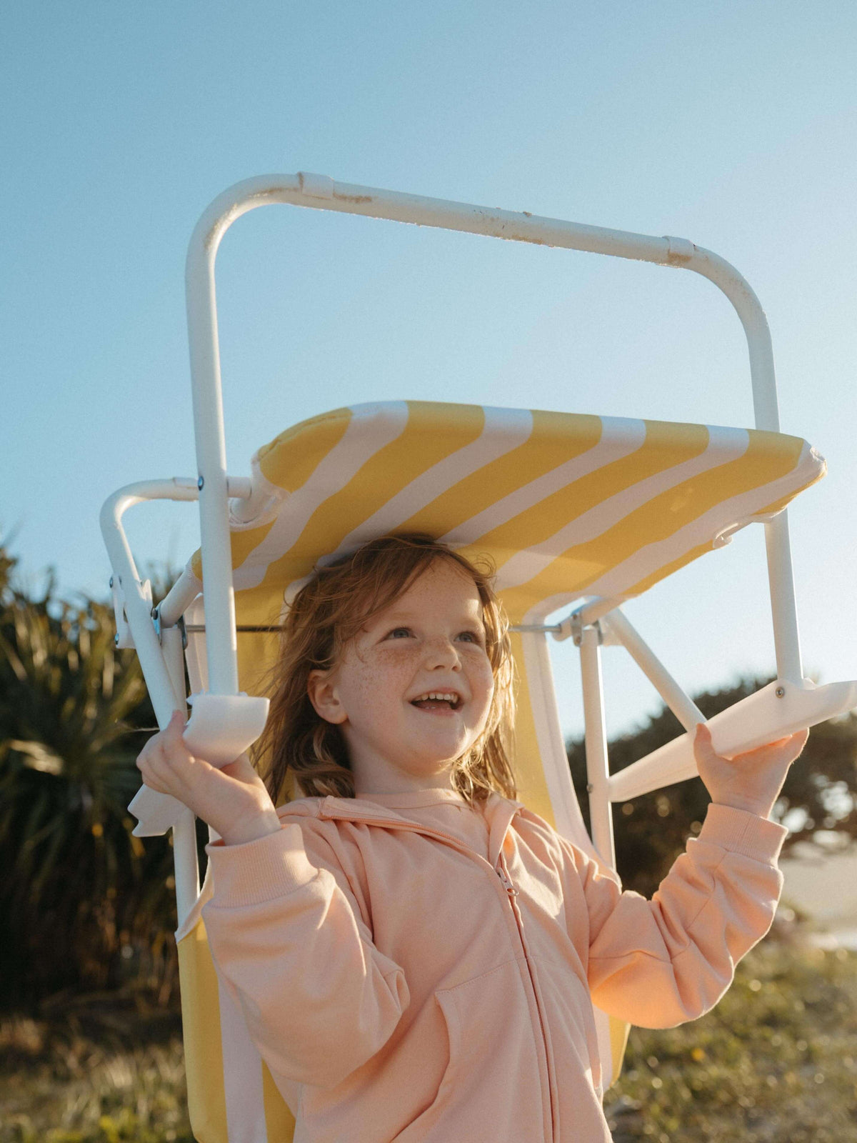 Girl holding a beach chair wearing a pink hoodie on a sunny day